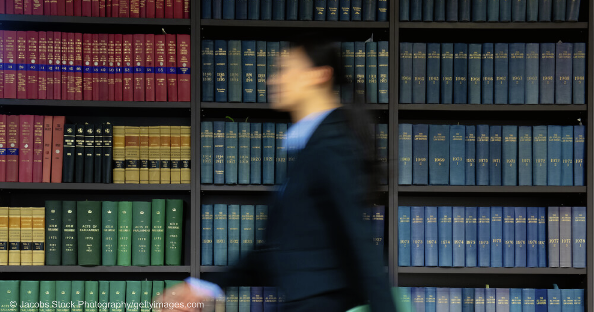 Eine verschwommene Frau geht vor einem großen Bücherregal entlang