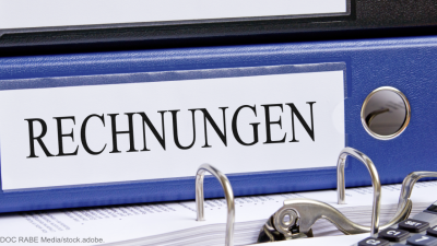 Ein Ordner mit der Beschriftung "Rechnungen" liegt zwischen Papier und einem Taschenrechner auf einem Tisch