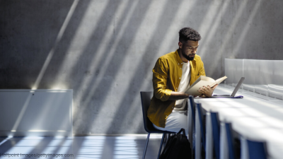 Ein junger Mann sitzt an einem langen Tisch und liest ein Buch